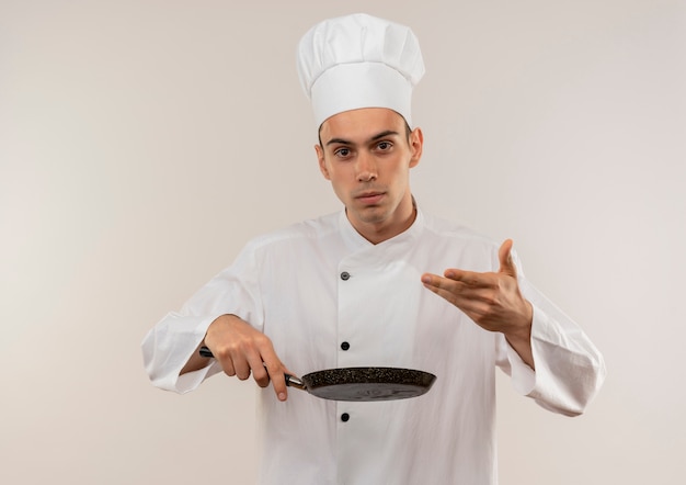 Young male cook wearing chef uniform holding poêle à frire sur mur blanc isolé