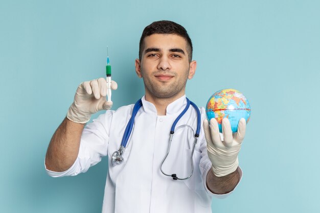 Young male doctor in white suit with blue stethoscope holding injection
