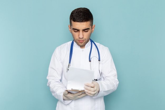 Young male doctor in white suit with blue stethoscope holding notepad