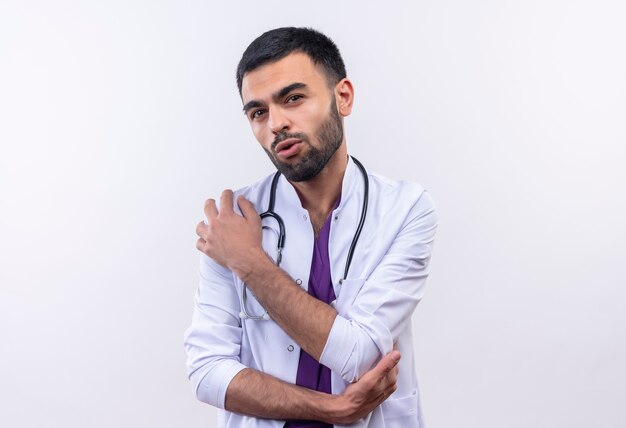 Young male doctor wearing stethoscope medical gown mis sa main sur l'épaule sur mur blanc isolé