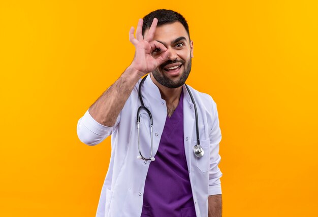 Young male doctor wearing stethoscope medical gown montrant look geste sur mur jaune isolé