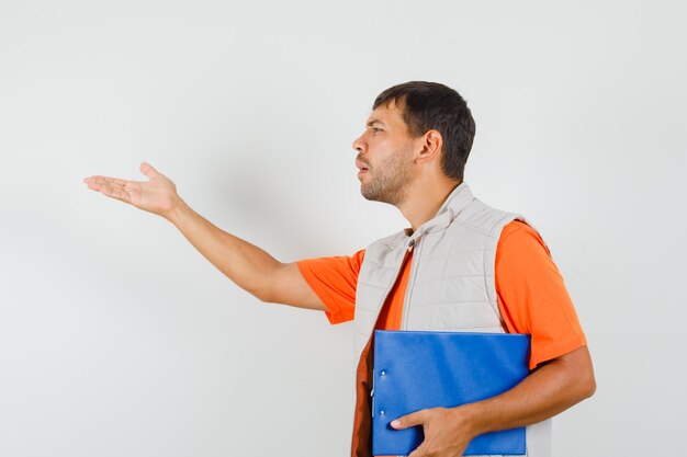 Young male holding clipboard, faisant poser la question signe en t-shirt, veste et à la confusion