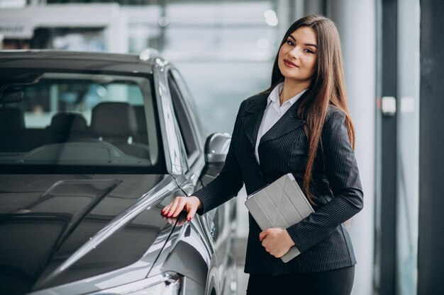 Young sales woman at carshowroom debout près de la voiture