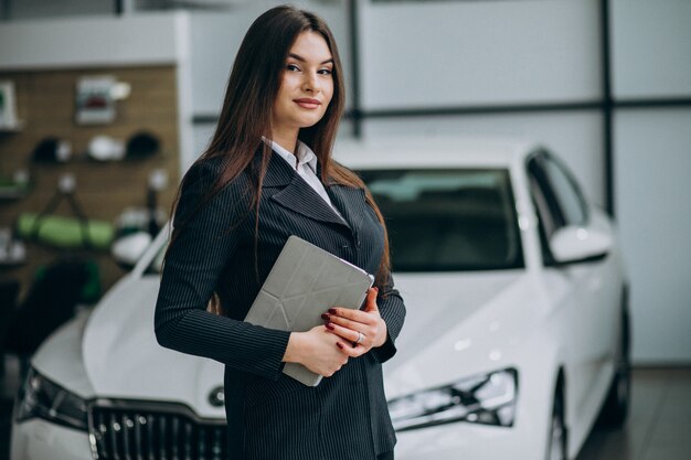 Young sales woman at carshowroom debout près de la voiture