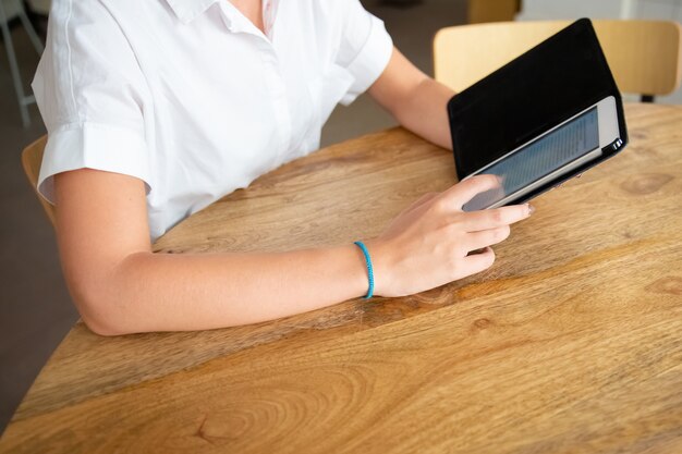 Young woman wearing white shirt, using tablet in open flip case, reading text on screen while sitting at table