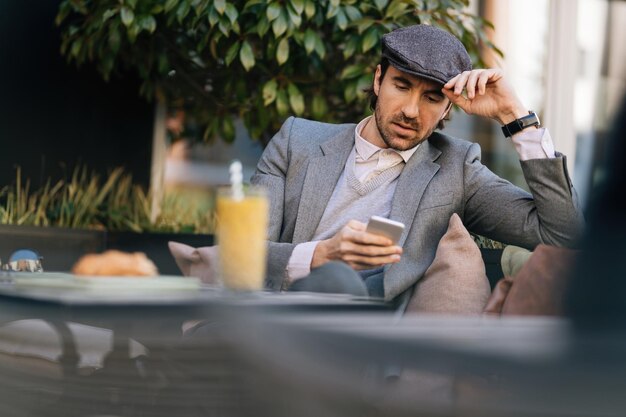 Yung entrepreneur lisant un message texte sur un téléphone portable assis dans un café en plein air