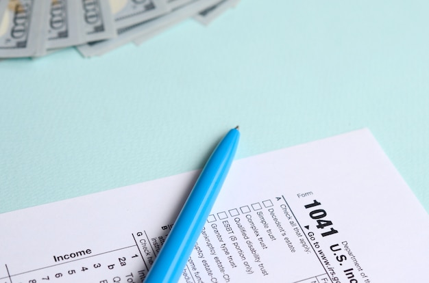 1041 formulaire d&#39;impôt se trouve près de cent dollars et stylo bleu sur un bleu clair