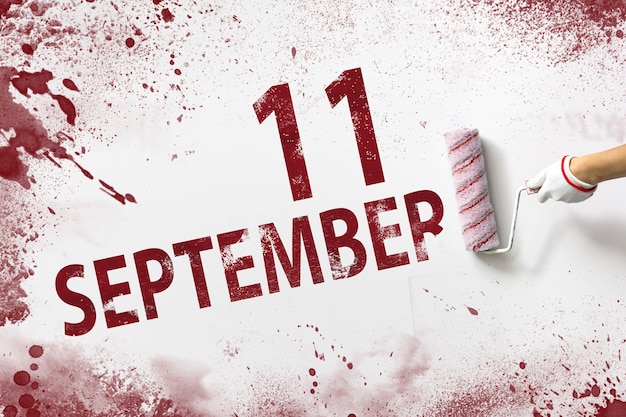11 septembre. Jour 11 du mois, date du calendrier. La main tient un rouleau avec de la peinture rouge et écrit une date calendaire sur fond blanc. Mois d'automne, concept de jour de l'année.