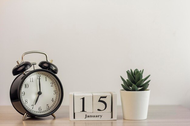 Le 15 janvier sur un calendrier en bois, à côté d'un réveil rétro et d'une succulente dans un mini pot sur une table lumineuse.Un jour de janvier.Jour d'hiver.Une copie de l'espace.Lieu de travail.