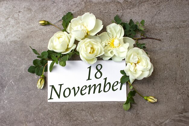 18 novembre. Jour 18 du mois, date du calendrier. Bordure de roses blanches sur fond gris pastel avec date du calendrier. Mois d'automne, concept de jour de l'année.