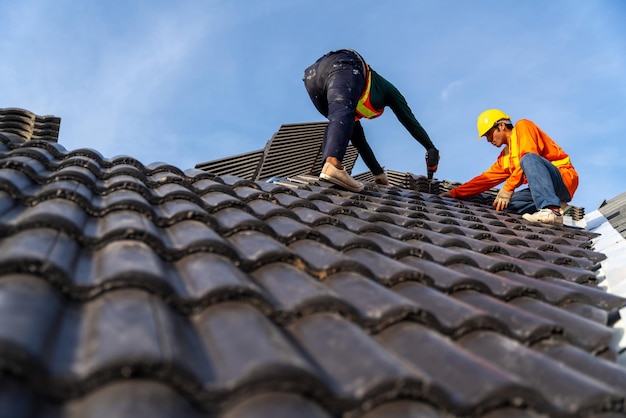 2 couvreurs travaillant sur le travail en hauteur pour installer les tuiles en béton sur le nouveau toit de la nouvelle construction de bâtiments modernes