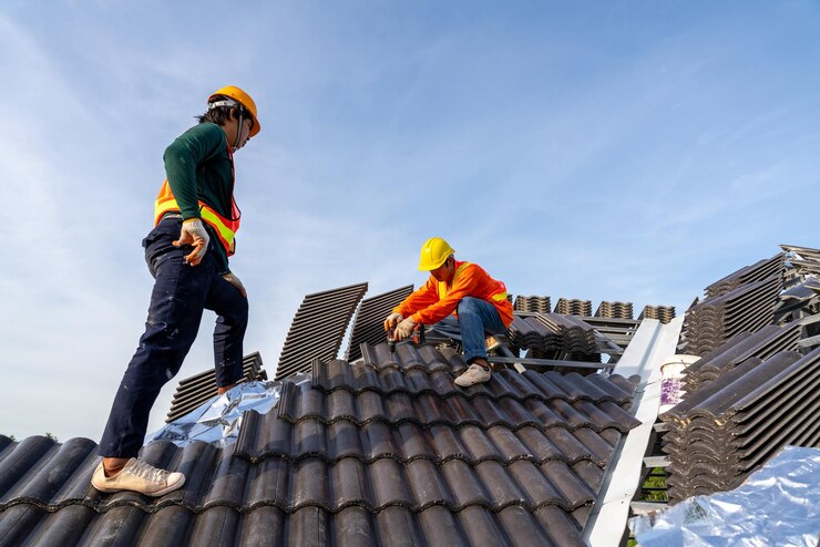 2 travailleurs de la construction installent un nouveau toit sur le chantier de construction Perceuse électrique utilisée sur de nouveaux toits avec des tuiles en béton Concept de bâtiment résidentiel en construction