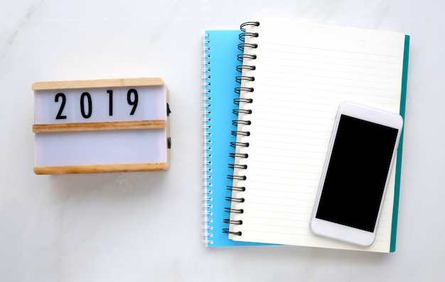 Photo 2019 sur une boîte en bois, un papier vierge pour ordinateur portable et un téléphone intelligent avec écran blanc