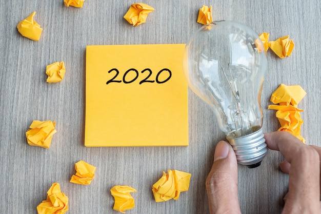 2020 mots sur une note jaune et un papier émietté avec ampoule