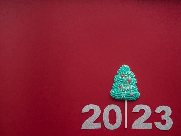 2023 et bonbon bleu sous forme d'arbre de Noël sur un fond rouge