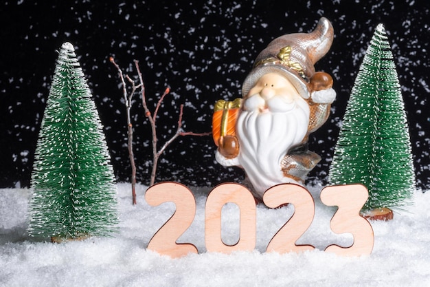 2023 New Year's Eve Toy Santa Claus avec des cadeaux dans la forêt enneigée parmi les arbres de Noël la nuit