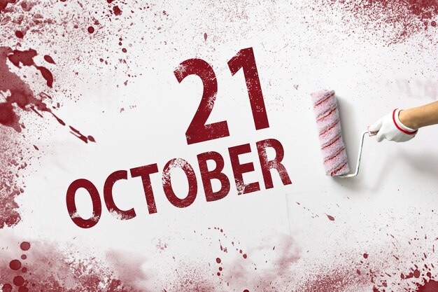 21 octobre. Jour 21 du mois, date du calendrier. La main tient un rouleau avec de la peinture rouge et écrit une date calendaire sur fond blanc. Mois d'automne, concept de jour de l'année.