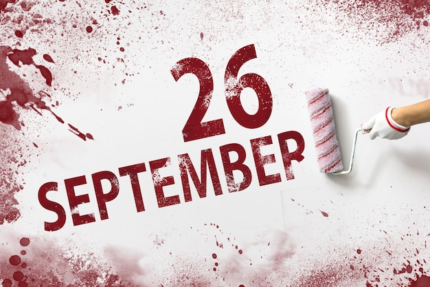 26 septembre. Jour 26 du mois, date du calendrier. La main tient un rouleau avec de la peinture rouge et écrit une date calendaire sur fond blanc. Mois d'automne, concept de jour de l'année.