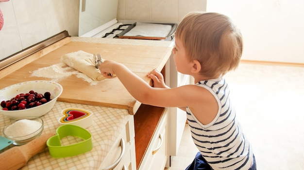 3 ans tout-petit garçon rouler la pâte sur planche de bois et cuire des biscuits pour le petit déjeuner