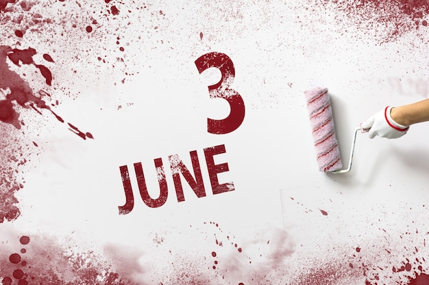 3 juin. Jour 3 du mois, date du calendrier. La main tient un rouleau avec de la peinture rouge et écrit une date calendaire sur fond blanc. Mois d'été, concept de jour de l'année.