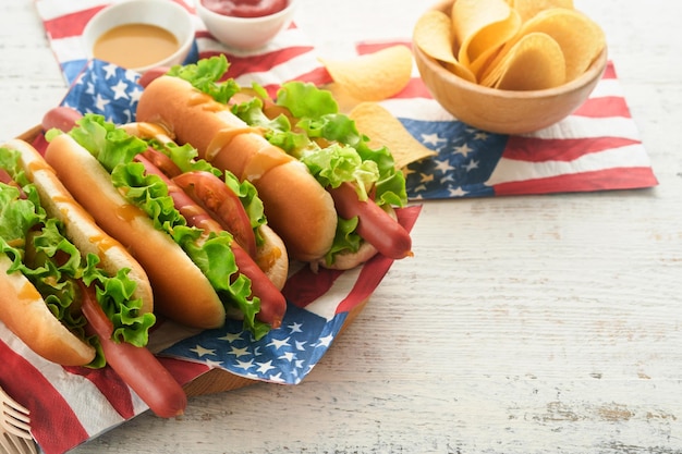 4 juillet Jour de l'Indépendance américaine Nourriture de pique-nique traditionnelle Hot-dog avec chips et cocktail Drapeaux américains et symboles des États-Unis Vacances de pique-nique patriotique sur fond en bois blanc Vue de dessus