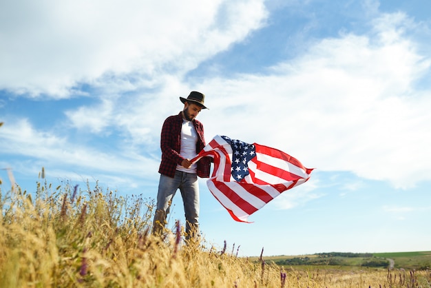 4 juillet. Le quatre juillet. Américain avec le drapeau national. Drapeau américain. Le jour de l'indépendance. Fête patriotique. L'homme porte un chapeau, un sac à dos, une chemise et un jean.