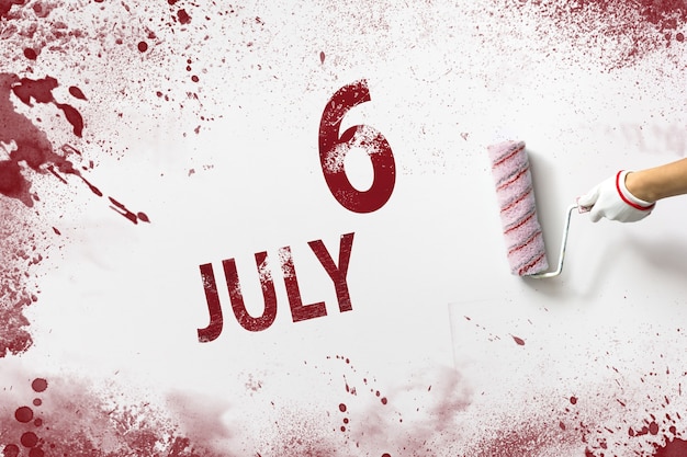 6 juillet. Jour 6 du mois, date du calendrier. La main tient un rouleau avec de la peinture rouge et écrit une date calendaire sur fond blanc. Mois d'été, concept de jour de l'année.