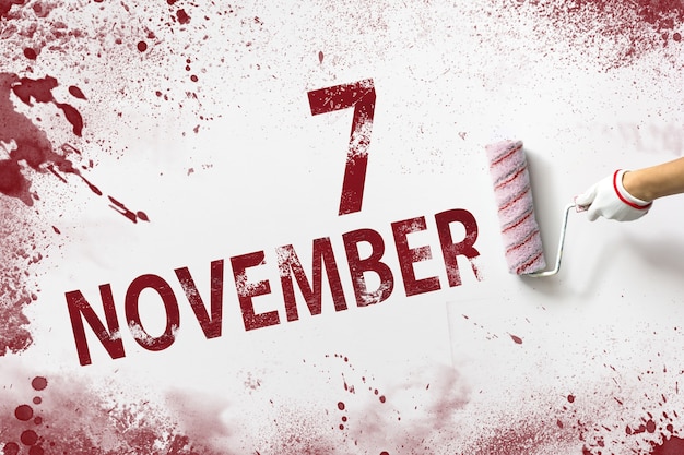 7 novembre. Jour 7 du mois, date du calendrier. La main tient un rouleau avec de la peinture rouge et écrit une date calendaire sur fond blanc. Mois d'automne, concept de jour de l'année.
