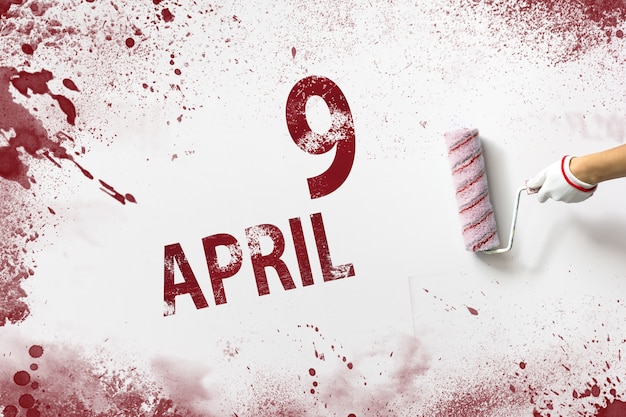 9 avril. Jour 9 du mois, date du calendrier. La main tient un rouleau avec de la peinture rouge et écrit une date calendaire sur fond blanc. Mois du printemps, concept du jour de l'année.