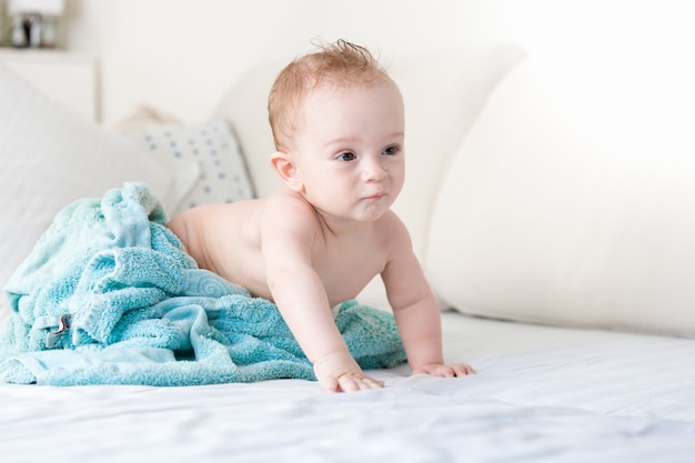 9 mois bébé garçon sous une serviette bleue sur le lit avec des draps blancs