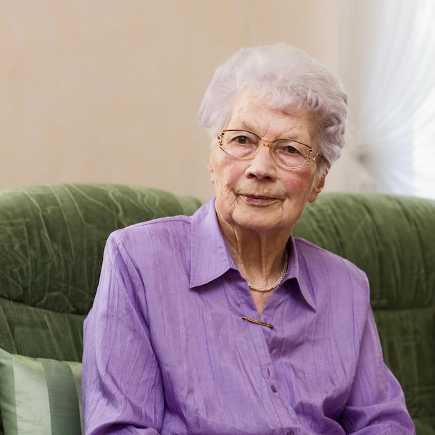 91 ans, femme assise sur un canapé dans son salon, portrait