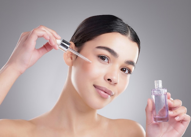 Ça me garde jeune Portrait en studio d'une jolie jeune femme appliquant du sérum facial sur un fond gris