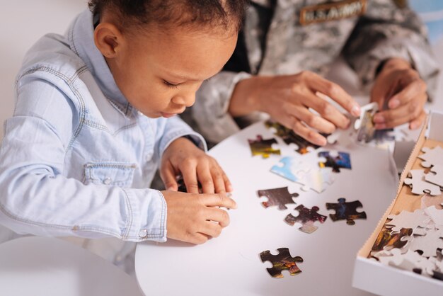 Ça rentre. Fille intelligente créative diligente aidant sa mère à terminer un grand puzzle tout en profitant de leur passe-temps commun pendant le week-end à la maison