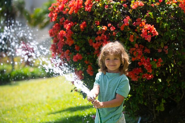 Aadorable enfant garçon arrosant les plantes du tuyau d'arrosage avec un tuyau d'eau dans le jardin à l'arrière-cour