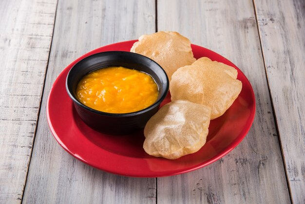 Aam Ras Puri est une délicieuse recette indienne servie comme dessert de saison, Aamras est une purée ou pulpe de mangue nature, servie dans un bol et une assiette en céramique sur un fond coloré ou en bois. Mise au point sélective