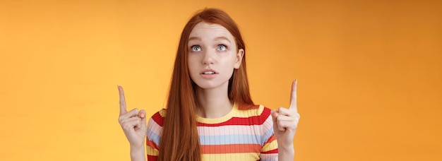 Abasourdie ravie jeune femme rousse axée sur les pairs pointant vers le haut l'index vers le haut regarde concentré