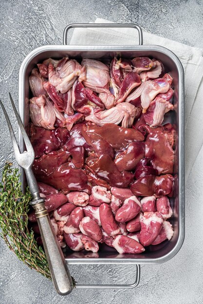 Abats de poulet cru ensemble de viande gésiers estomacs foie et coeurs dans un plateau en acier avec des herbes Fond blanc Vue de dessus