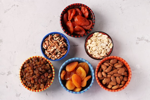Abricot séché, raisins secs, arachides, amandes, noix dans des bols sur table en béton gris