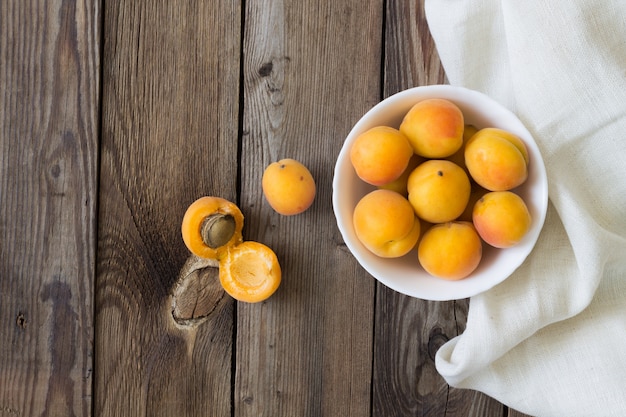 Abricots frais dans un bol blanc sur une table en bois avec une serviette de cuisine. Espace copie