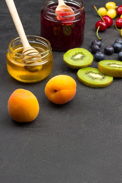 Abricots Kiwi, cerise, pots de miel et confiture sur surface noire. Vue de dessus. Copier l'espace