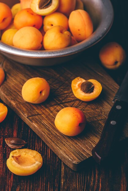 Photo abricots moelleux avec un couteau sur une vieille planche à découper en bois et un bol en métal avec des fruits