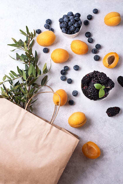 Abricots mûrs, myrtilles, mûres éparpillées sur fond blanc, achat de baies d'été, sac en papier et abricots, myrtilles.