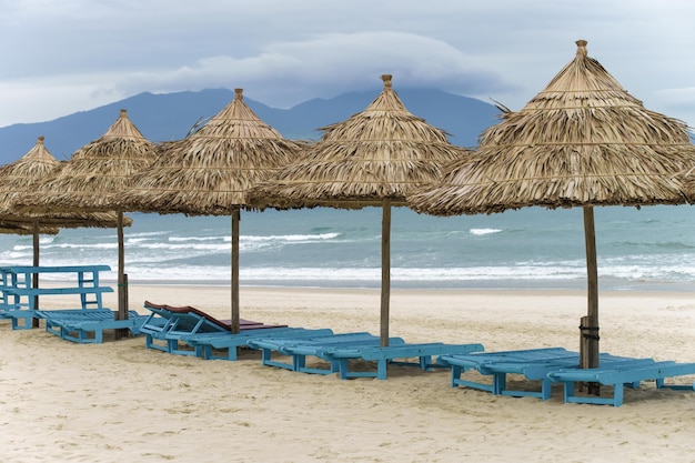 Abris de palmiers et chaises longues à China Beach à Da Nang, Vietnam. Elle est aussi appelée plage de Non Nuoc. Mer de Chine méridionale et montagnes de marbre en arrière-plan.