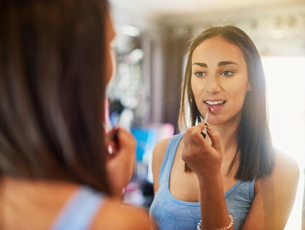 Accentuant ses lèvres déjà parfaites Photo d'une jolie jeune femme appliquant du brillant à lèvres dans un miroir à la maison