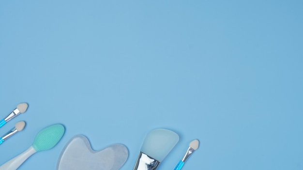 Accessoires cosmétiques sur fond bleu pinceaux de maquillage éponges pour appliquer des cosmétiques décoratifs brosse de lavage masseur de pierre de gouache pour le motif de gros plan du visage avec des cosmétiques vue de dessus à plat