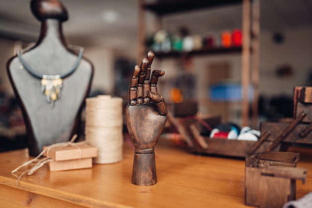 Accessoires de couture, main en bois et mannequin avec bijouterie artisanale sur la table en atelier, gros plan. Bijoux faits à la main