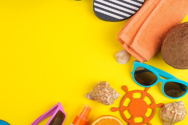 Accessoires d'été avec coquillages, lunettes de soleil, orange et noix de coco sur fond jaune vif. vue de dessus.