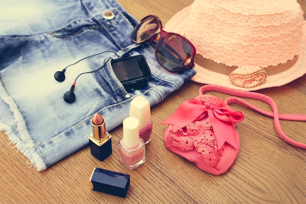 Accessoires d'été pour femmes: lunettes de soleil, perles, shorts en jean, téléphone portable, écouteurs, chapeau de soleil, sac à main, rouge à lèvres, vernis à ongles. Image tonique
