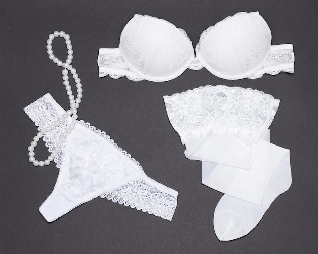 Accessoires femmes. Ensemble de lingerie blanche, bas de dentelle, collier de perles sur fond gris