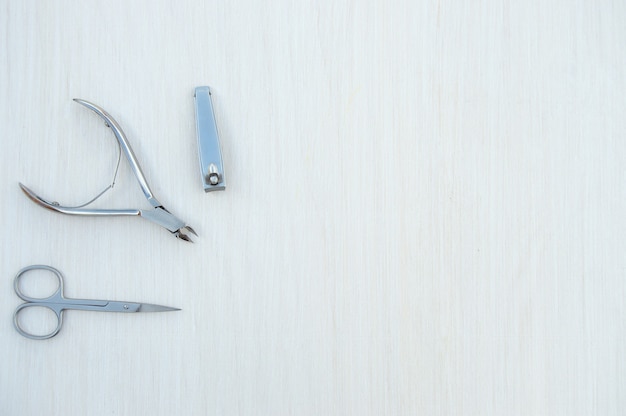 accessoires en métal pour manucure sur un fond en bois blanc vue de dessus à plat